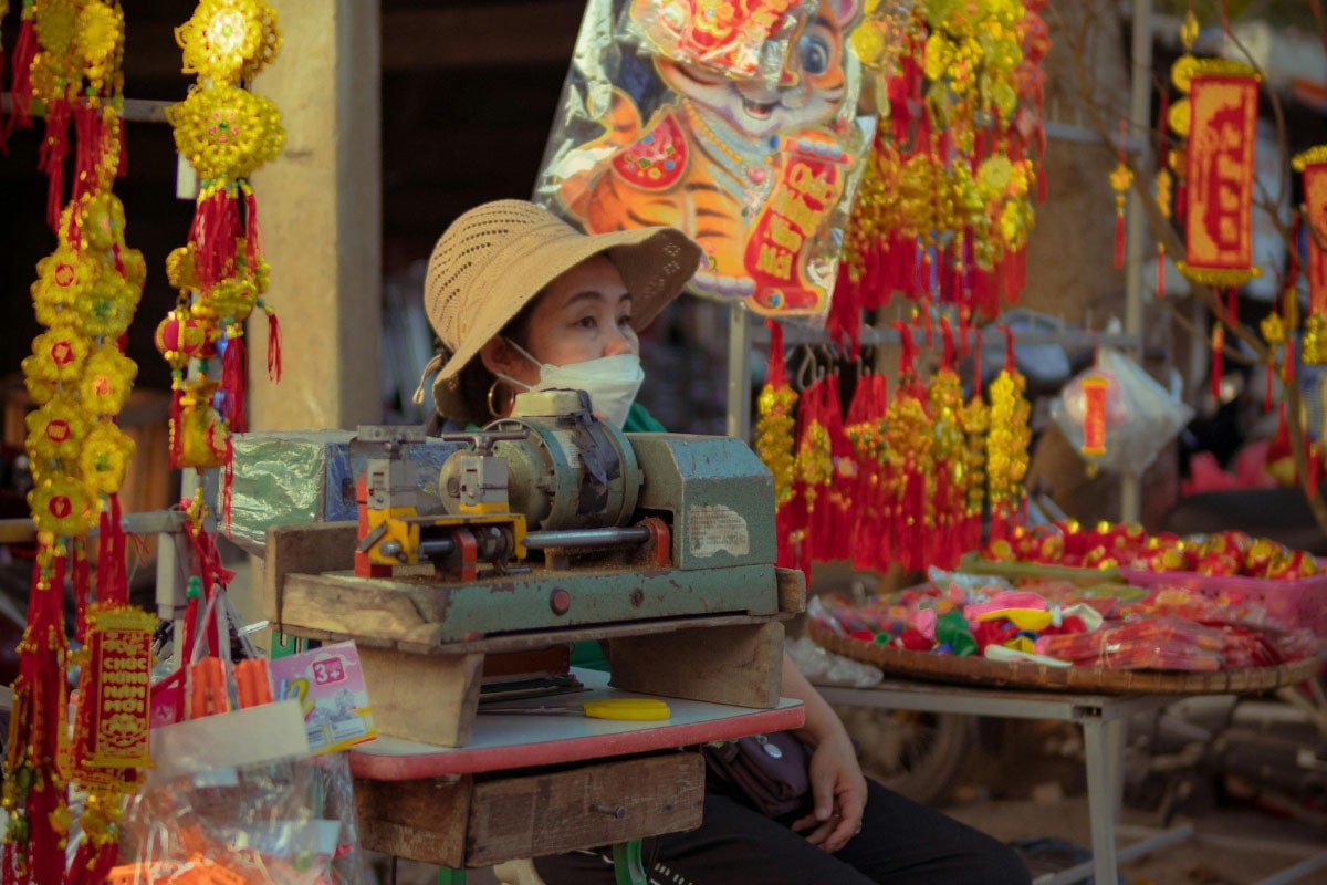 Photograph of a woman wearijng a mask selling brightly coloured decorations at a stall in Asia